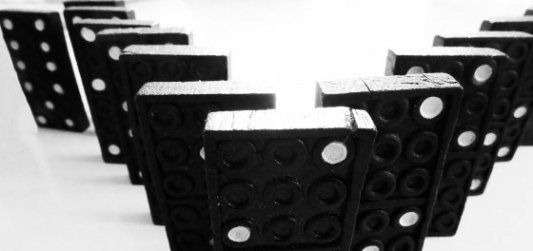 Fila de fichas de dominó negras y blancas dispuestas en V a punto de caer