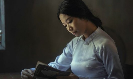 Joven mujer leyendo un libro en una habitación de luz suave.