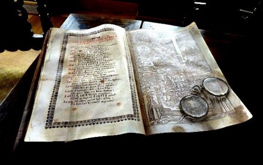 Libro antiguo iluminado junto a unas viejas gafas redondas.