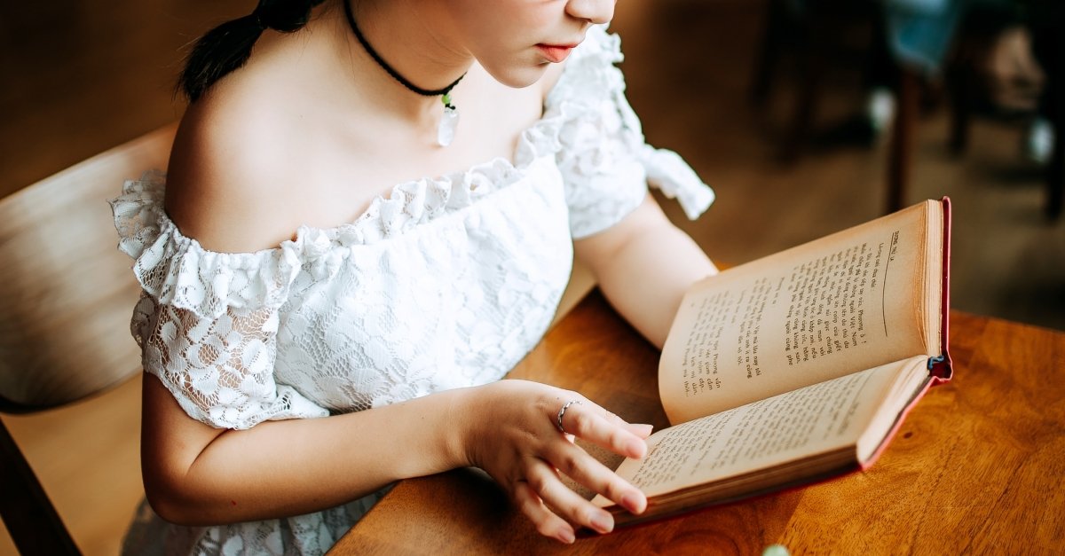 Mujer con una blusa veraniega blanca leyendo un libro sobre una mesa de madera