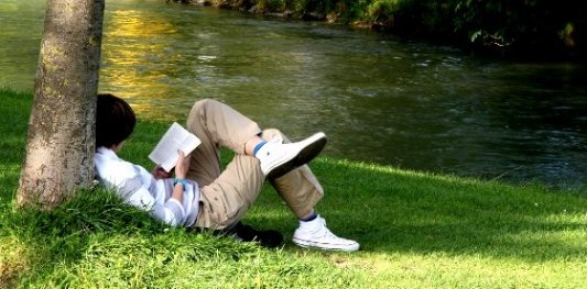 Joven sentado junto a un lago leyendo tranquilamente un libro