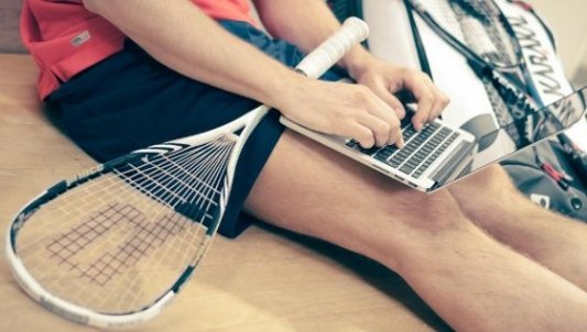 Deportista con raqueta escribiendo en un portátil.