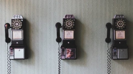 Tres viejos teléfonos vintage sobre una pared de papel pintado.