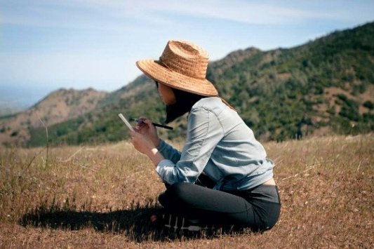 Imagen de una chica sentada en el campo escribiendo en un cuaderno.