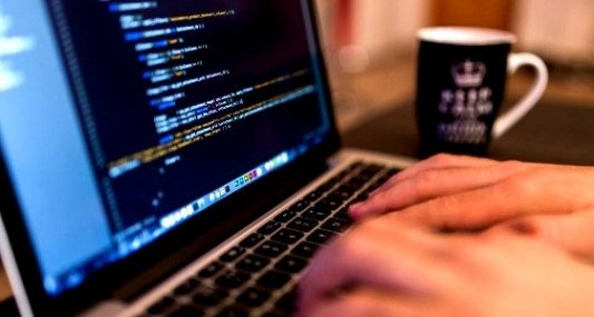 Programador trabajando delante del ordenador con una taza de café.