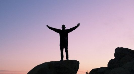 Hombre subido a una roca mirando al cielo en plena libertad.