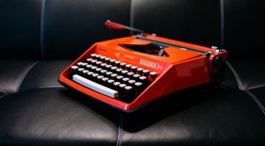 Máquina clásica de escribir de color rojo sobre sillón de cuero negro.