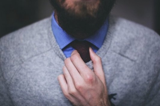 Imagen de un joven con barba ajustando la corbata.