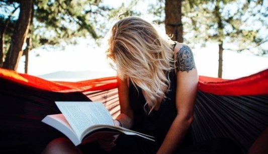 Joven mujer leyendo un libro en una hamaca.
