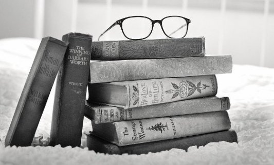 Pila de libros viejos con unas gafas de pasta encima.