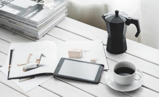 Mesa de trabajo con café, revistas y una tableta.