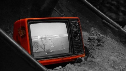 Vieja televisión de tubo de color naranja abandonada en el suelo.