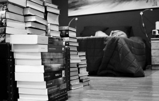 Cama rodeada de libros en blanco y negro.