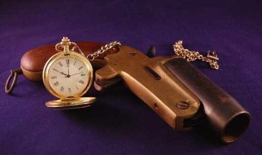 Pistola antigua junto a un reloj dorado de bolsillo.
