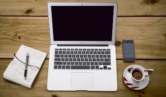 Ordenador portátil con un bloc de notas, teléfono y taza de café.