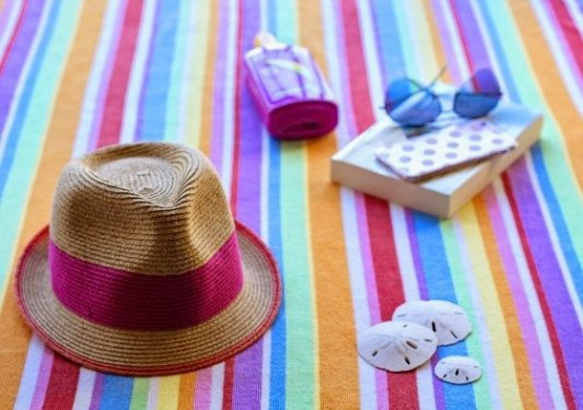 Sombrero, toalla, gafas de sol y un libro en la playa.