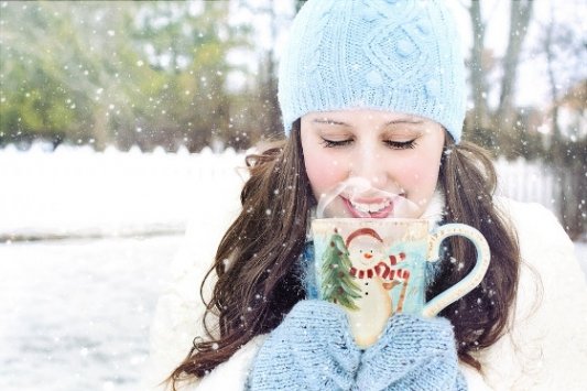 Chica joven en la nieve bebiendo chocolate.