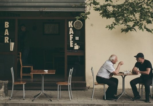 Un anciano y un hombre conversando en la terraza de un bar