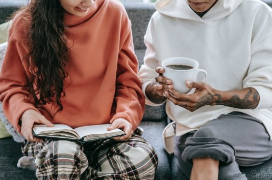 Dos personas reunidas, una con un café y otra con un libro