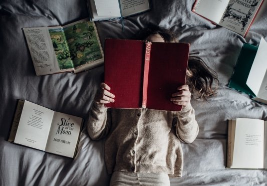 Chica leyendo en una cama cubierta de libros