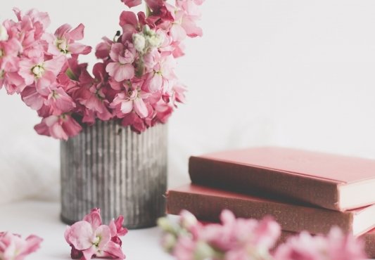 Libros apilados al lado de una maceta con flores rosas