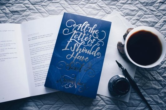 Libro con una portada azul y llamativa sobre un libro abierto y con una taza llena, una pluma y tinta al lado