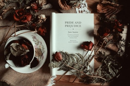Volumen abierto de Orgullo y Prejuicio en inglés y rodeado de una taza de té y flores secas=