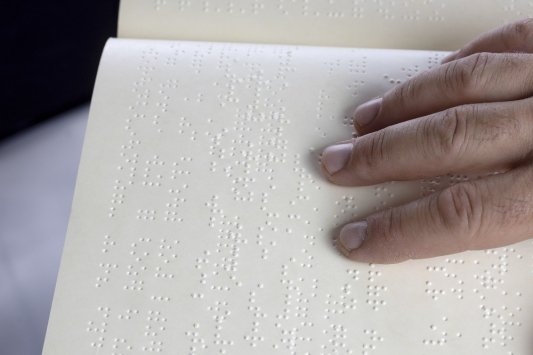 Dedos leyendo líneas impresas en sistema braille