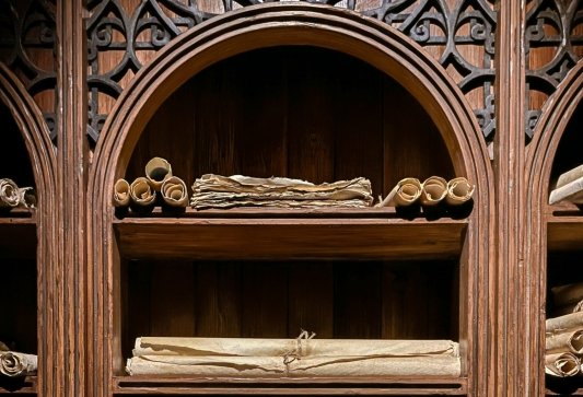 Estantería de madera con dos baldas y manuscritos antiguos presentados en rollos