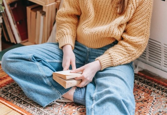 Fotografía de una chica en el suelo, con las piernas cruzadas y un libro al que le marca la página con un dedo