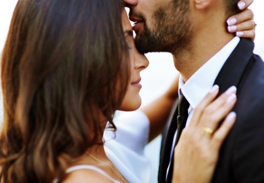 Fotografía de una pareja donde él le besa la frente mientras ella se apoya en su pecho 