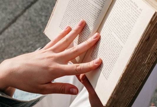 Imagen de una mano que se apoya en las páginas de un libro abierto mientras la otra sujeta el tomo