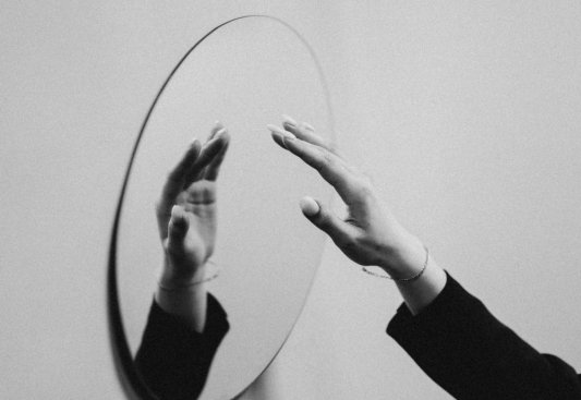 Fotografía en blanco y negro de una mano aproximándose a un espejo