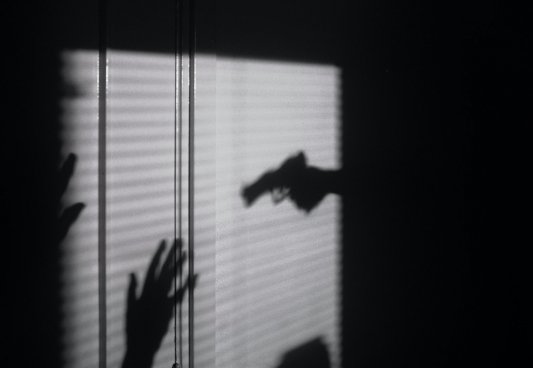 Sombras sobre una pared de una pistola apuntando a alguien con las mano alzadas