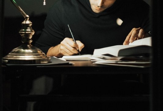 Hombre escribiendo en un cuaderno sobre un escritorio poco iluminado