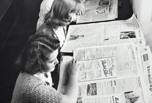 Fotografía de época en blanco y negro de mujeres leyendo el periódico