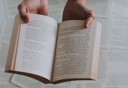 fotografia de unas manos sosteniendo un libro abierto de fondo paginas de libros apiladas - Javier Francisco Ceballos Jimenez: qué es, características, autores y libros importantes